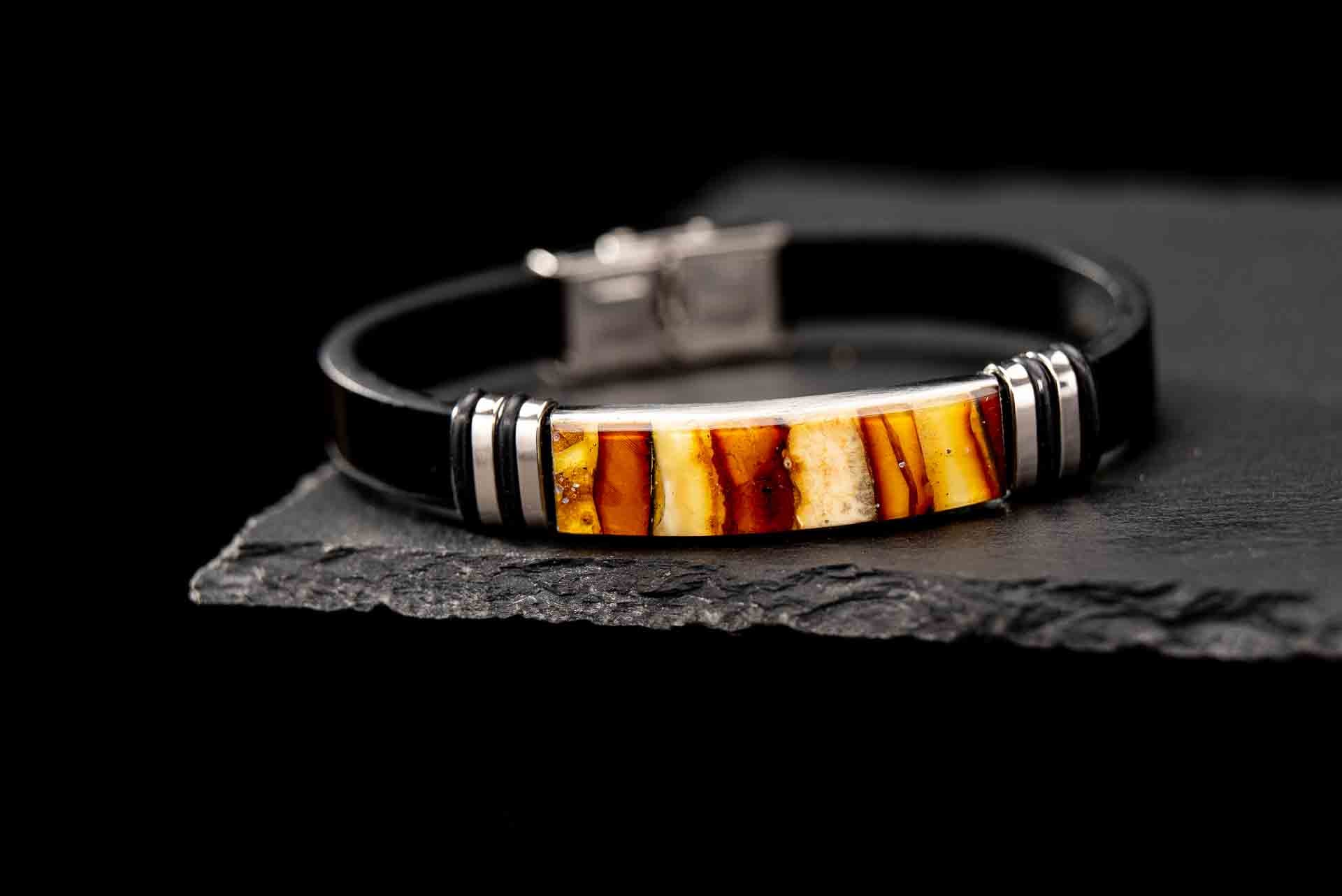 Handcrafted black genuine leather bracelet with real Baltic amber mosaic inlay centerpiece. Luxury unisex jewelry featuring silver-tone accents and secure lobster clasp, displayed on dark slate stone – premium amber bracelet for men and women.