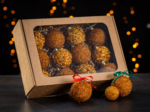 BalticBliss genuine Baltic amber Christmas tree ornament balls set—box of twelve handmade amber chip baubles in eco‑friendly kraft window gift packaging with shredded paper filler, displayed with red‑bow and green‑bow sample decorations in front—authentic Lithuanian amber holiday décor ships worldwide